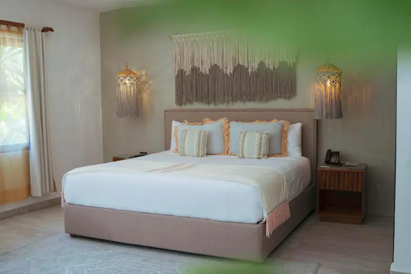 Une chambre lumineuse avec un grand lit recouvert d'une courtepointe blanche et de coussins.