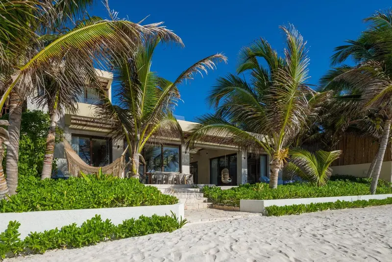 Bâtiment blanc bordé de végétation tropicale et de sable fin.
