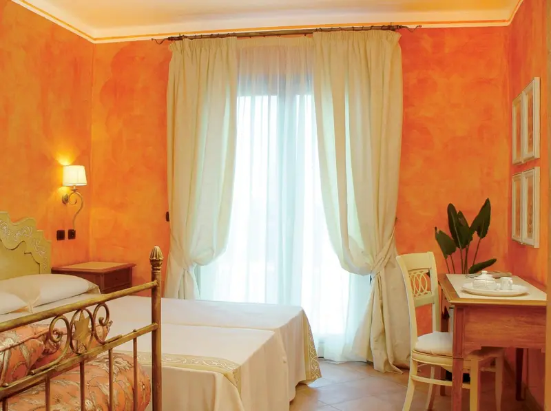 Une chambre lumineuse aux murs orange et aux rideaux clairs.