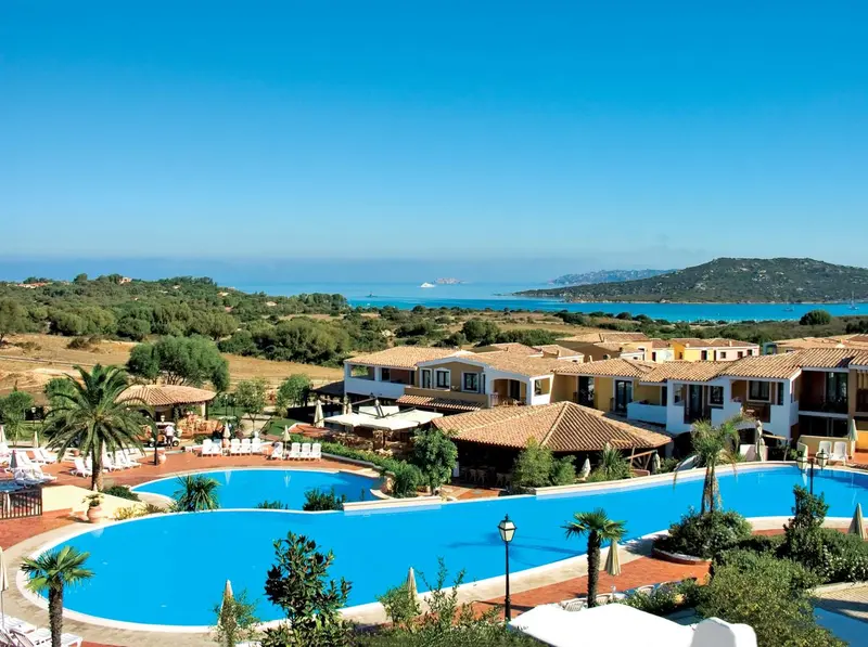 Vue aérienne d'un complexe hôtelier avec piscine et végétation luxuriante face à la mer.
