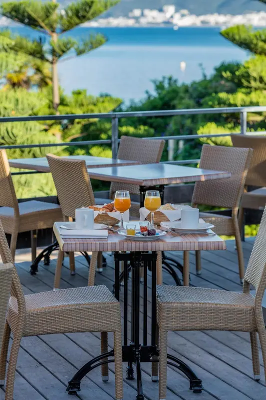 Une table est dressée pour le petit-déjeuner sur une terrasse ensoleillée avec vue sur la mer.