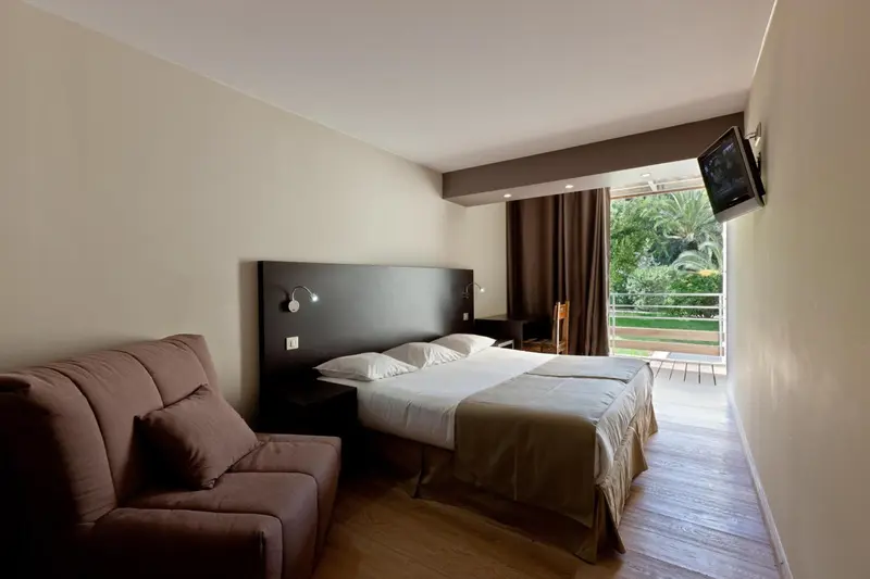 Une chambre lumineuse avec un lit double et un canapé face à une baie vitrée.
