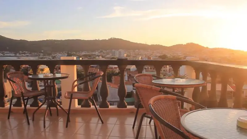 Terrasse avec tables et chaises offrant une vue sur la ville et les montagnes au coucher du soleil.