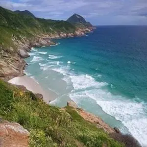 Cote rocheuse surplombant une plage de sable et une mer turquoise.