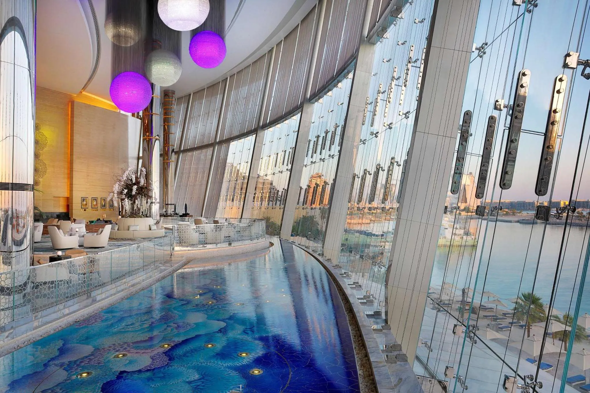 Une piscine intérieure s'étend le long d'une grande baie vitrée offrant une vue sur la mer.