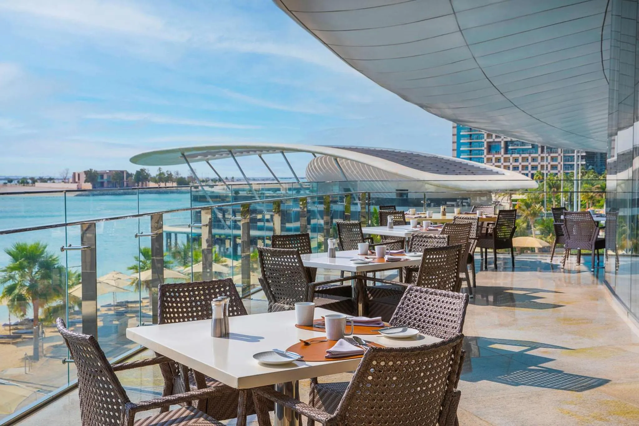 Terrasse ombragée avec tables et chaises donnant sur la mer.
