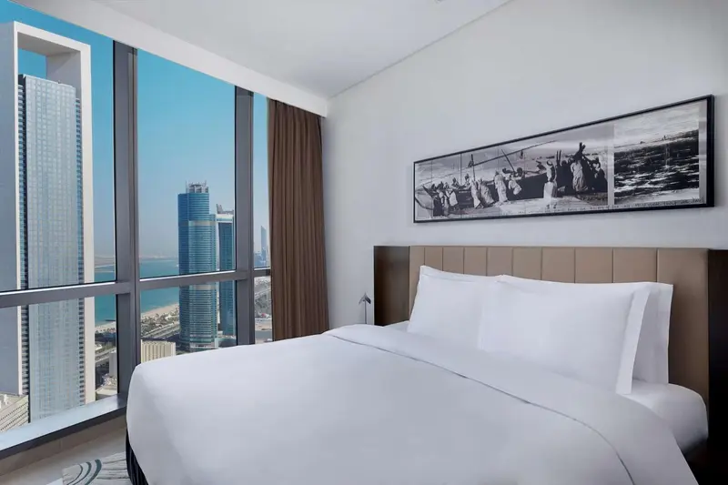 Chambre lumineuse avec un grand lit et une vue sur la ville.