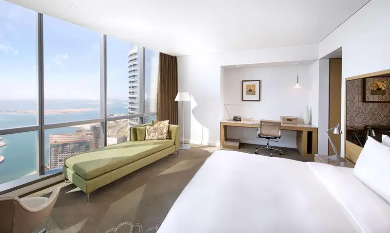 Chambre lumineuse avec un grand lit et un coin salon près d'une fenêtre panoramique.