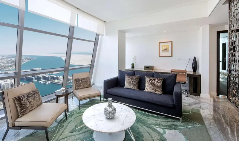 Un salon moderne avec canapé, fauteuils et vue sur la mer par de grandes fenêtres.