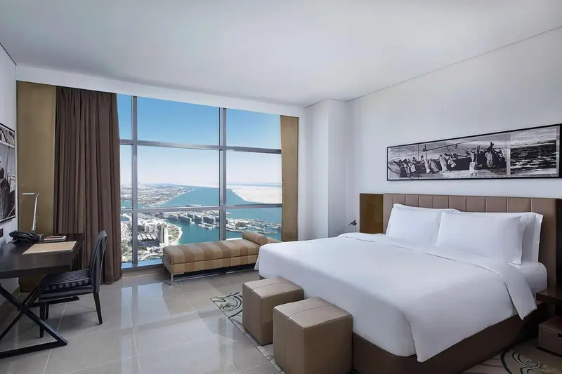 Chambre lumineuse avec un grand lit et une vue sur la ville et la mer.
