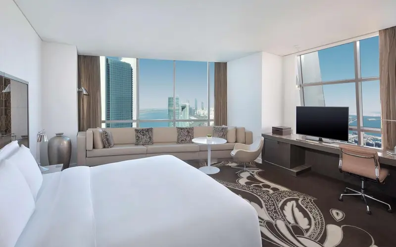 Chambre moderne avec un grand lit et un coin salon près d'une fenêtre panoramique.