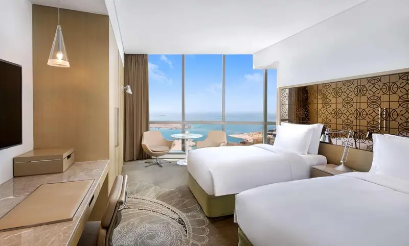 Chambre lumineuse avec deux lits et vue sur la mer.