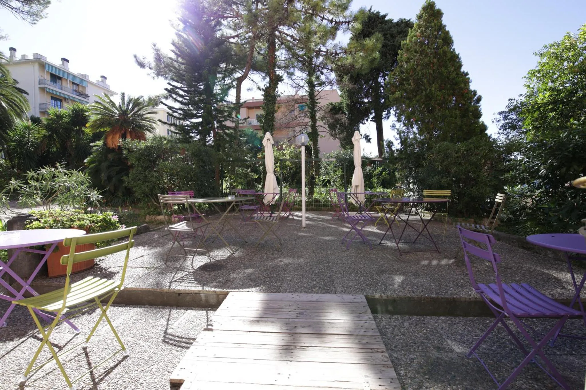 Terrasse ombragée avec tables et chaises colorées dans un jardin.