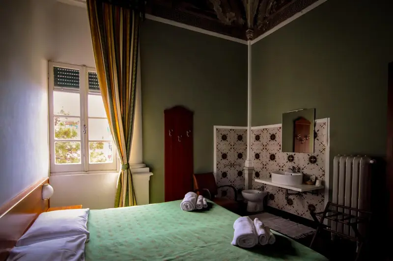 Une chambre lumineuse avec un lit recouvert d'une couverture verte et un coin lavabo décoré de carreaux.