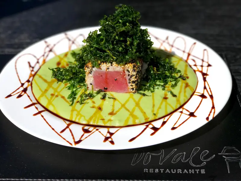 Assiette de poisson cru décorée de verdure et de sauce.