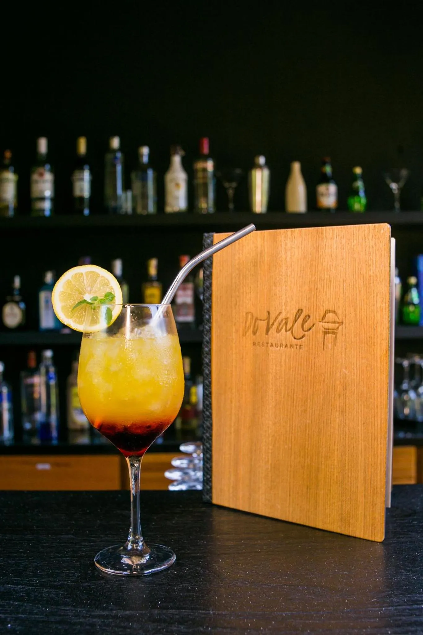 Un cocktail coloré est présenté devant un menu en bois sur un comptoir sombre.
