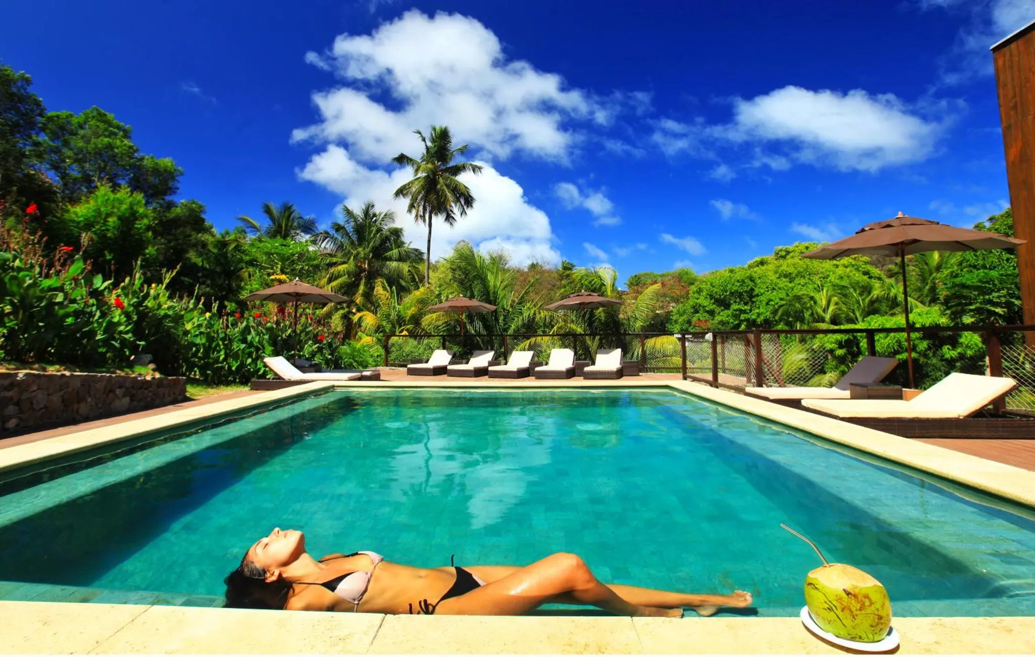 Une femme se relaxe au bord d'une piscine ensoleillée, entourée de végétation luxuriante.
