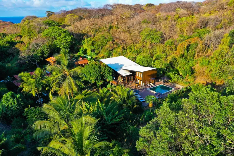 Vue aérienne d'un complexe hôtelier tropical avec piscine et végétation luxuriante.