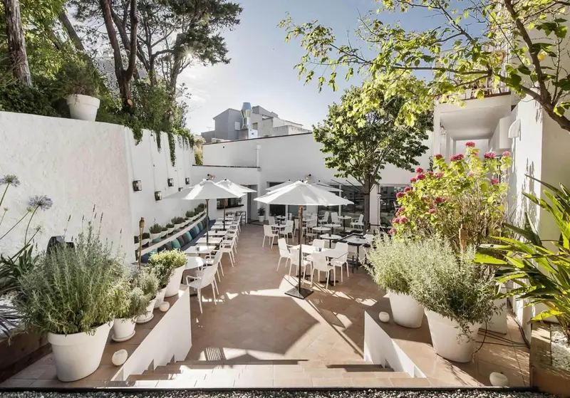 Terrasse ombragée avec tables et chaises blanches, entourée de végétation.