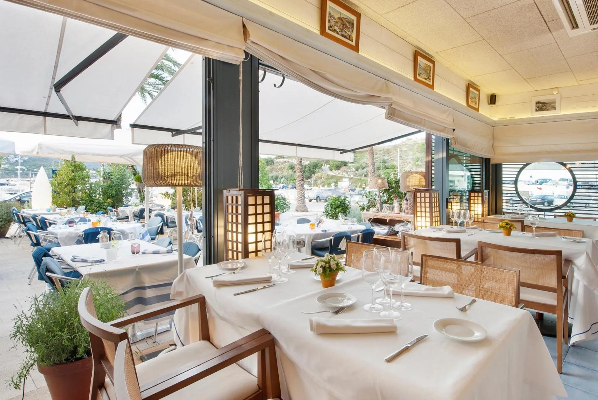 Une salle de restaurant lumineuse avec des tables dressées et une vue sur un port.