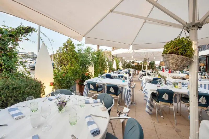 Tables dressées en terrasse avec une vue sur un port de plaisance.
