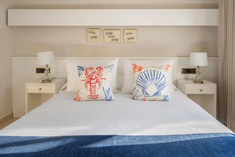 Lit double avec oreillers blancs et coussins décorés de motifs marins.
