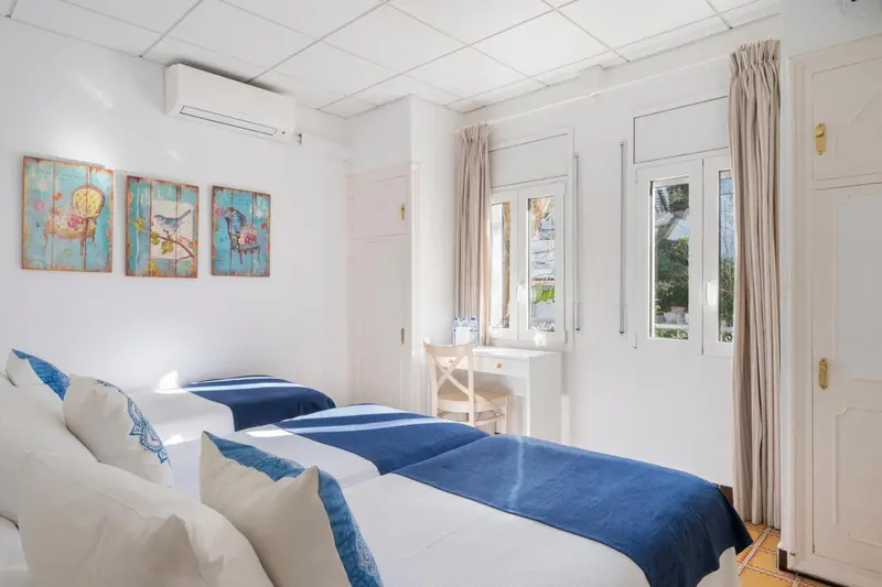 Une chambre lumineuse avec deux lits simples et un bureau près d'une fenêtre.