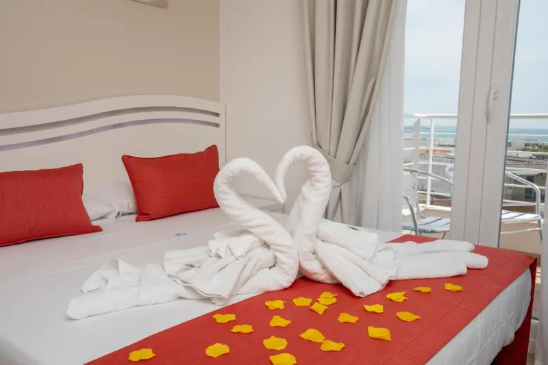 Lit double avec décoration en serviettes en forme de cygnes et pétales de fleurs sur un drap rouge.