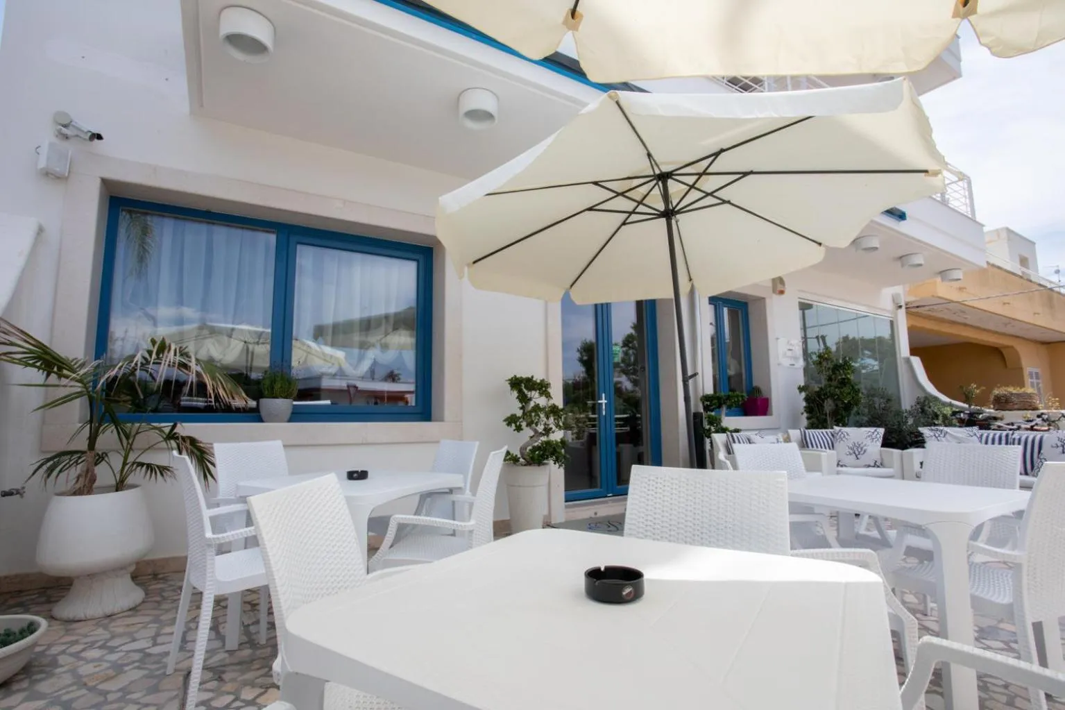 Terrasse ombragée avec tables et chaises blanches.