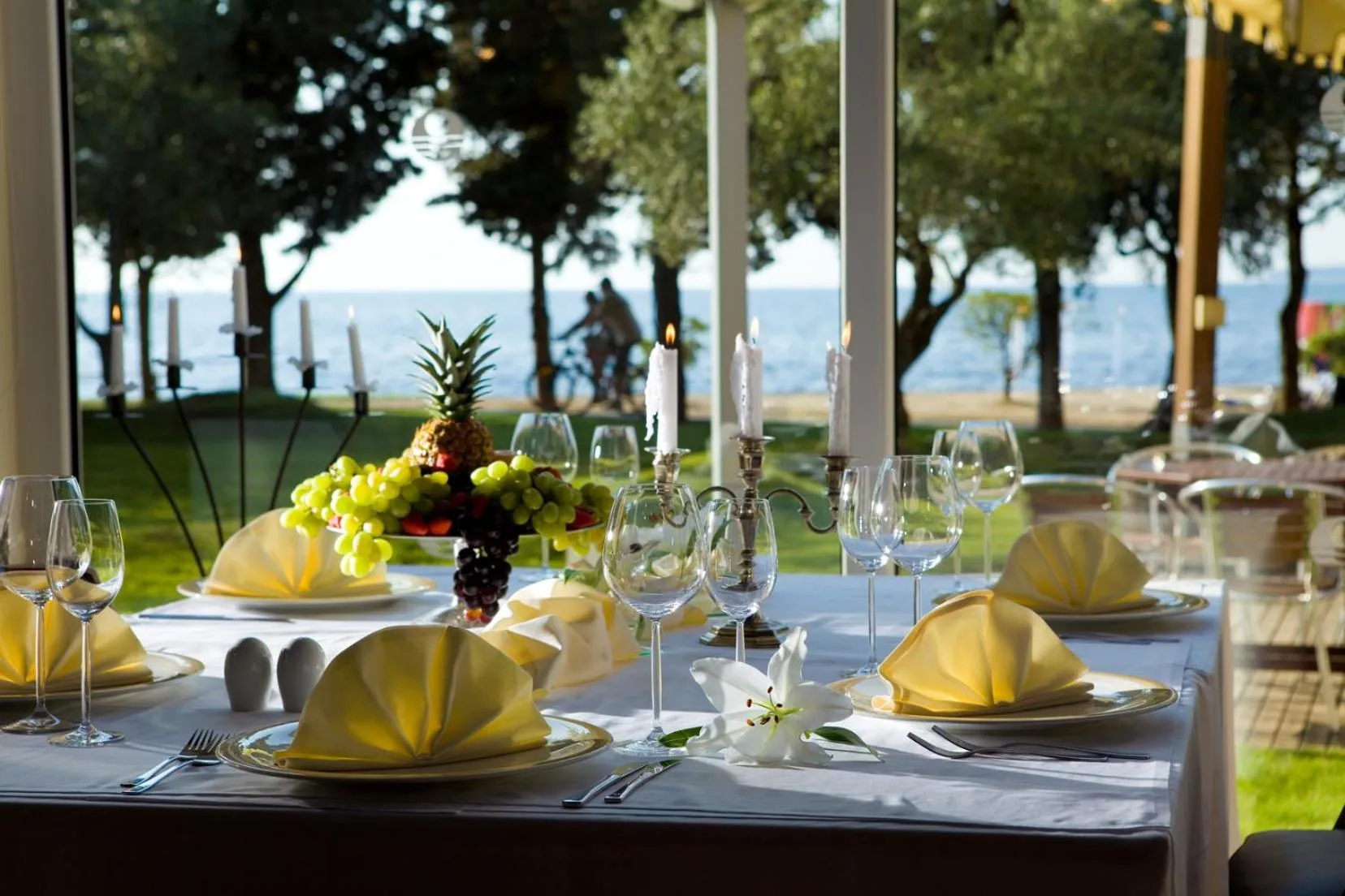 Une table dressée avec des verres, des couverts et des fruits frais, devant une vue sur la mer.