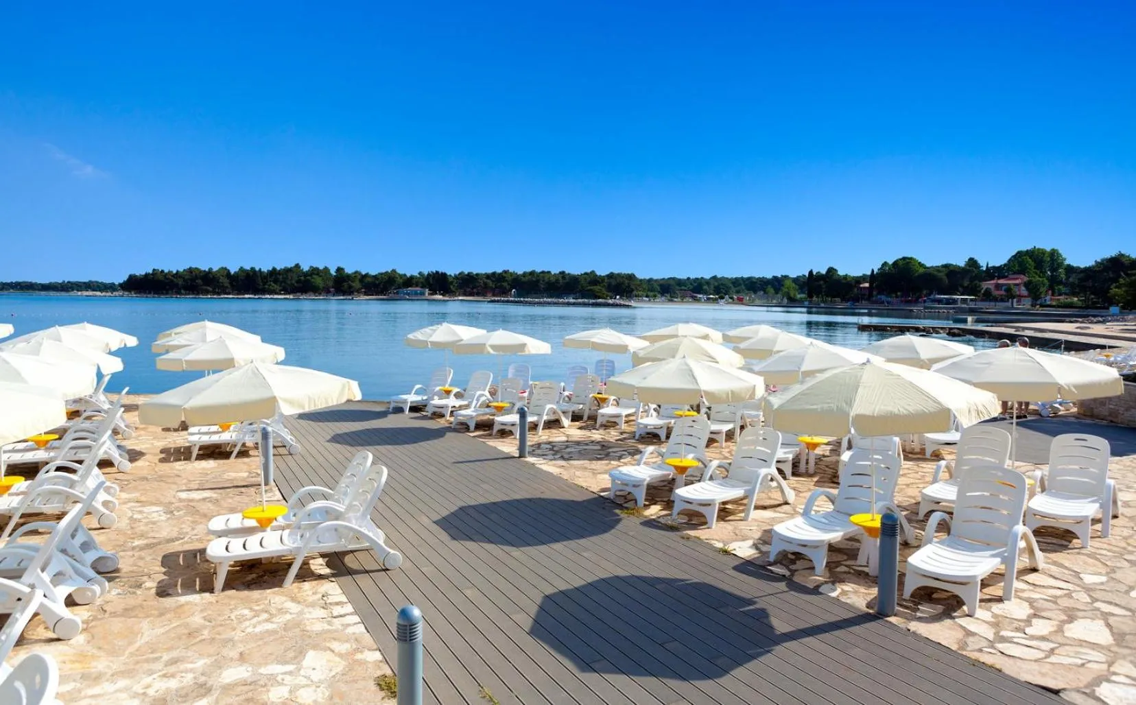 Transats blancs et parasols sur une terrasse en bois face à la mer.