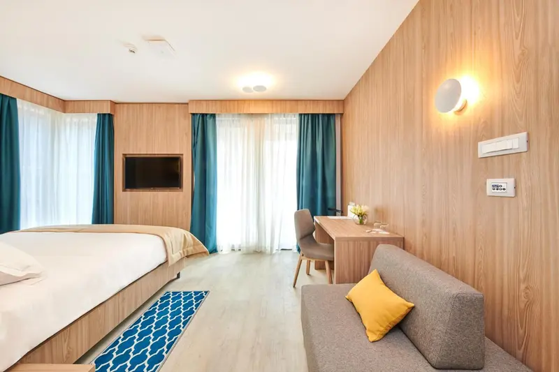 Chambre lumineuse avec un lit, un bureau et un coin salon.