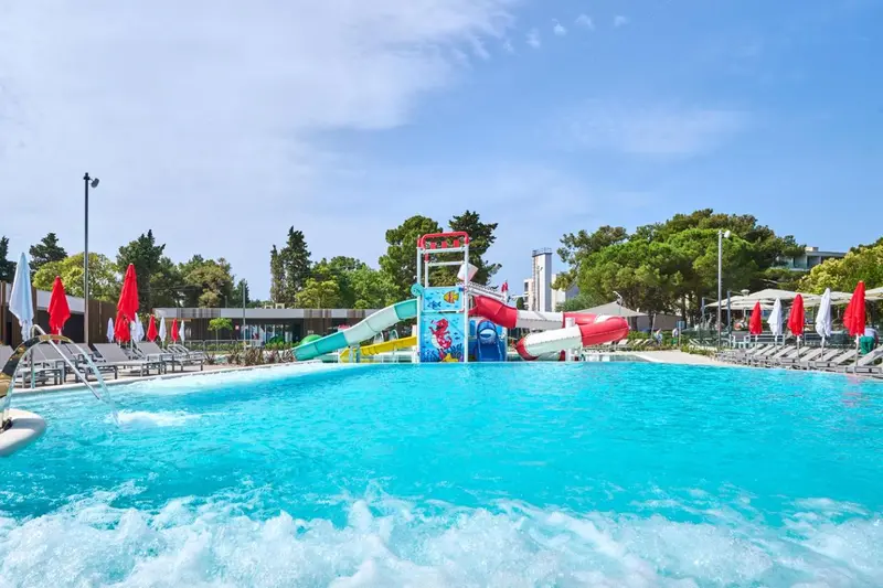 Une piscine avec un toboggan aquatique et des transats sous des parasols.