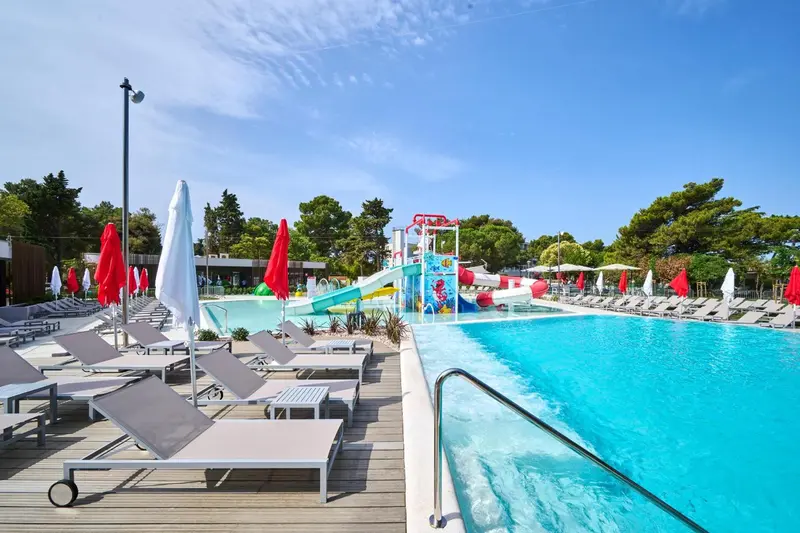 Transats et parasols bordent une piscine avec toboggans aquatiques.