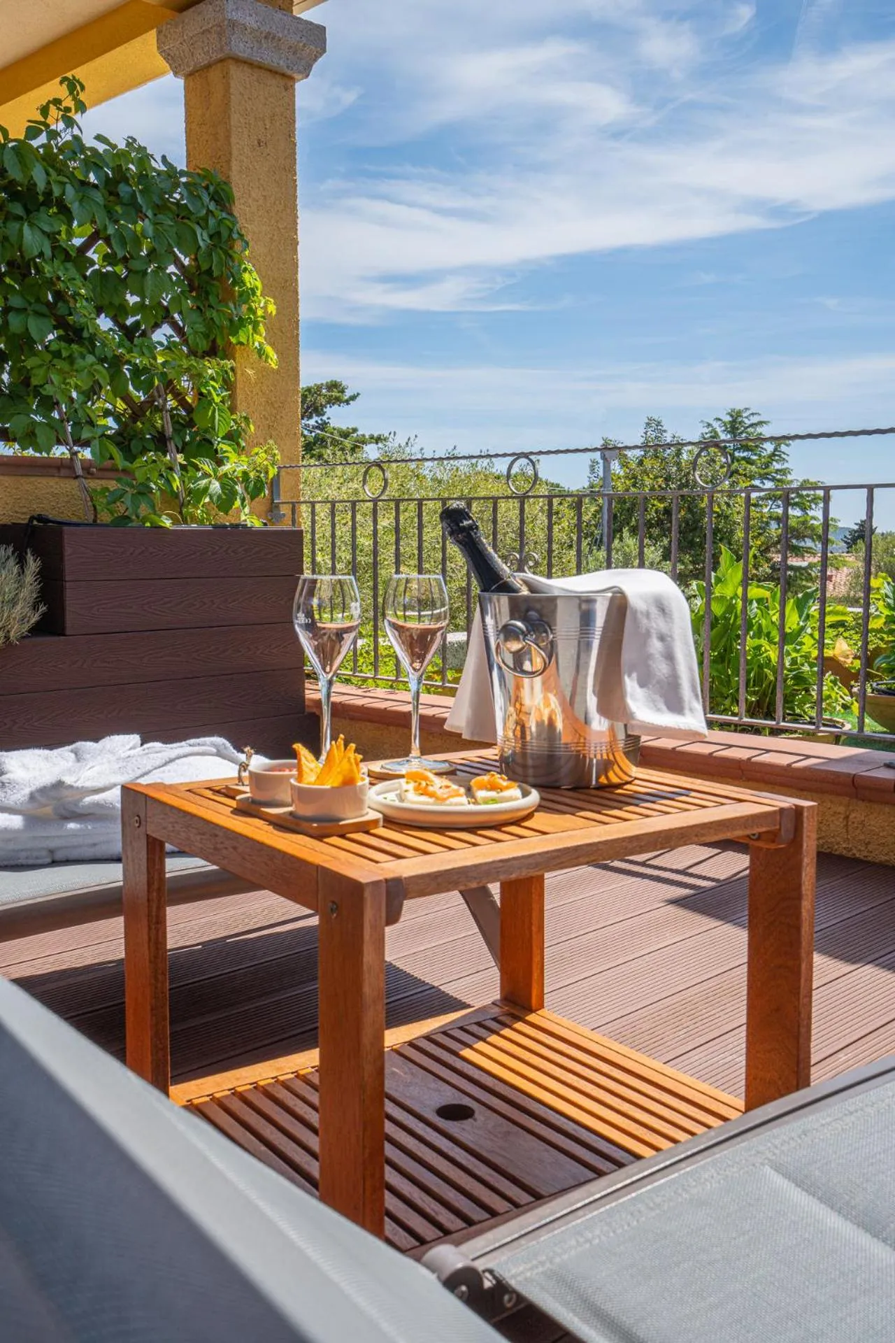 Une table en bois avec des boissons et des amuse-gueules sur une terrasse ensoleillée.