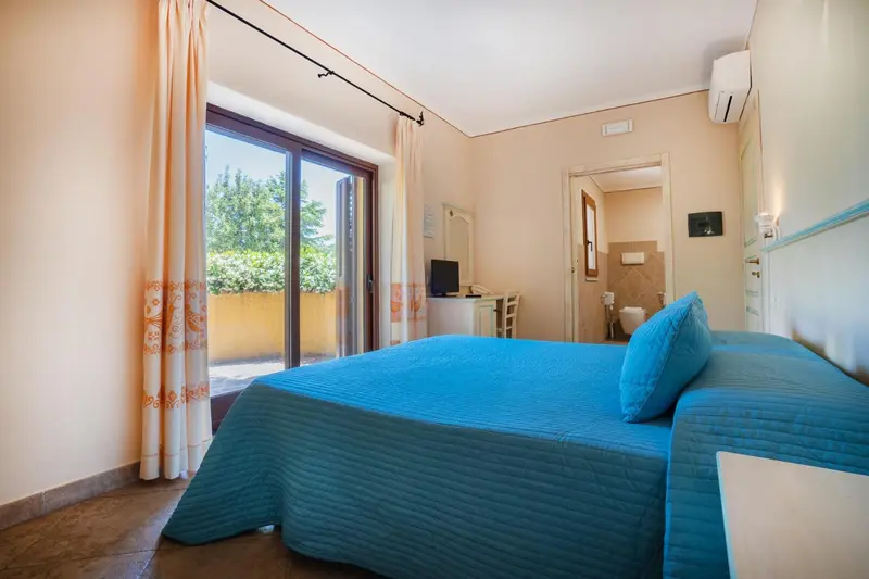 Chambre lumineuse avec un lit fait et une porte-fenêtre ouverte sur l'extérieur.