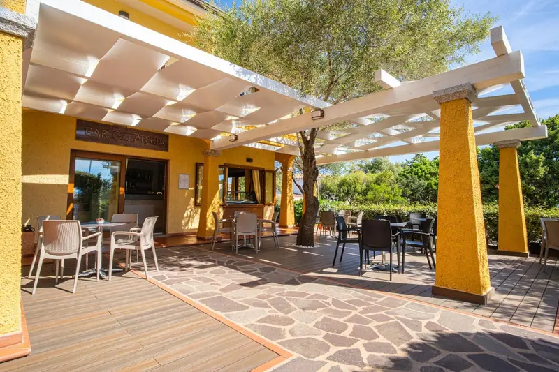 Terrasse ombragée avec tables et chaises près d'un bar.