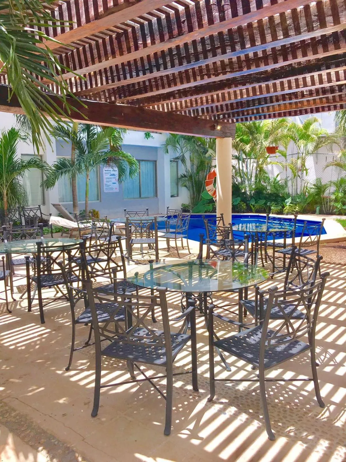 Terrasse ombragée avec tables et chaises près d'une piscine.