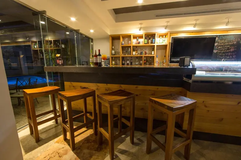 Un comptoir de bar en bois avec des tabourets hauts et des bouteilles.
