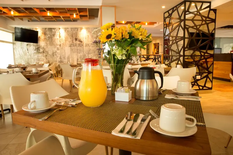 Une table de restaurant est mise avec des couverts, une carafe de jus d'orange et des tasses à café.