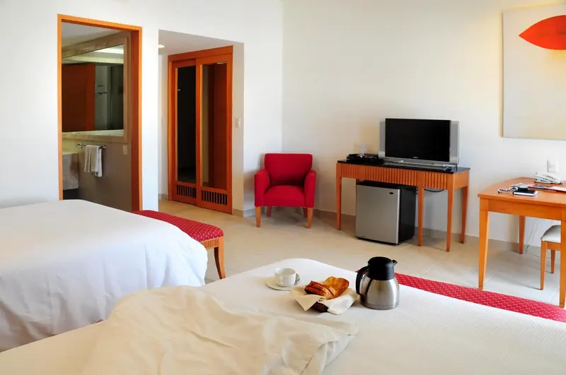 Une chambre lumineuse avec deux lits, un bureau et un fauteuil rouge.