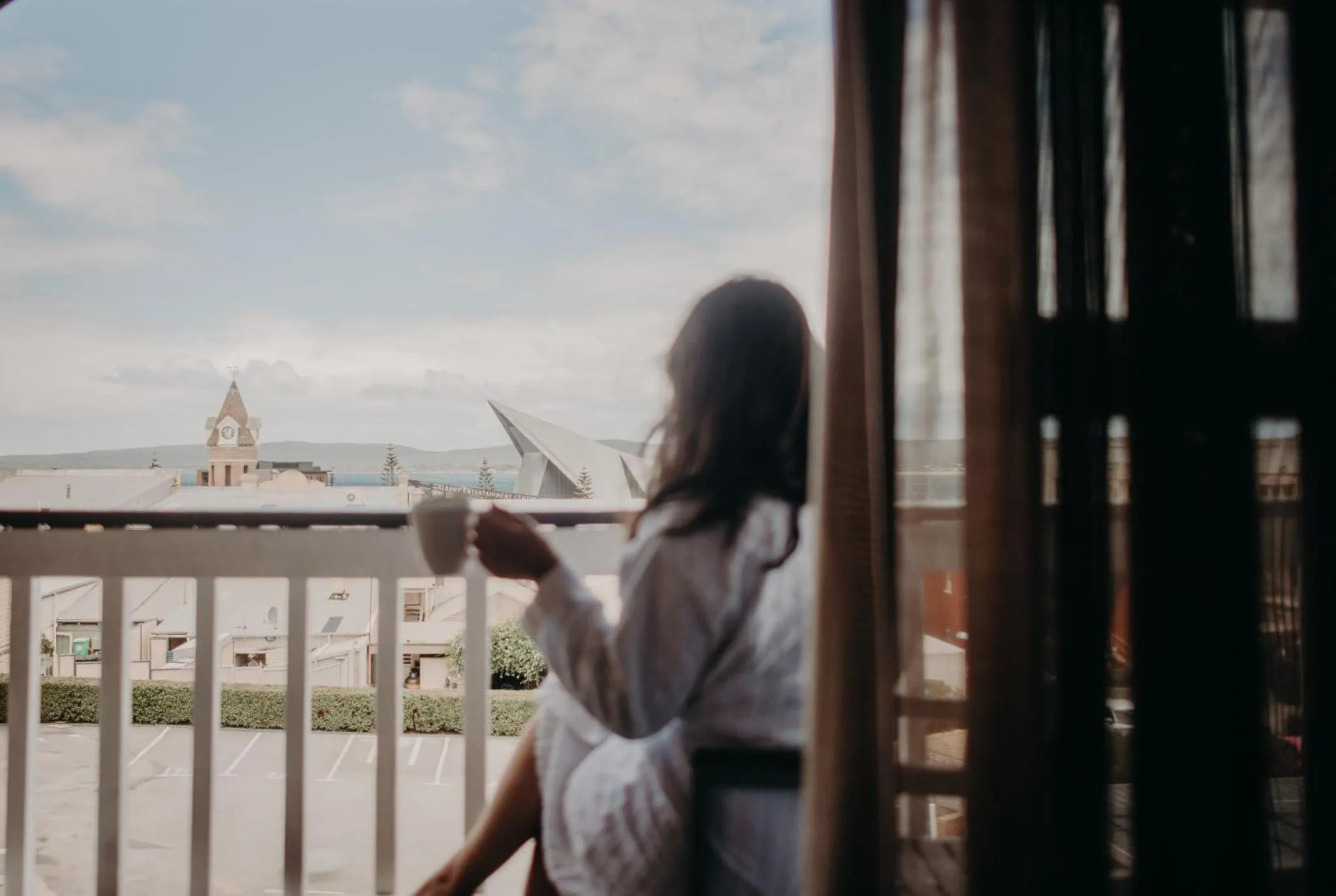 Une personne tient une tasse sur une terrasse ensoleillée avec vue sur la ville.
