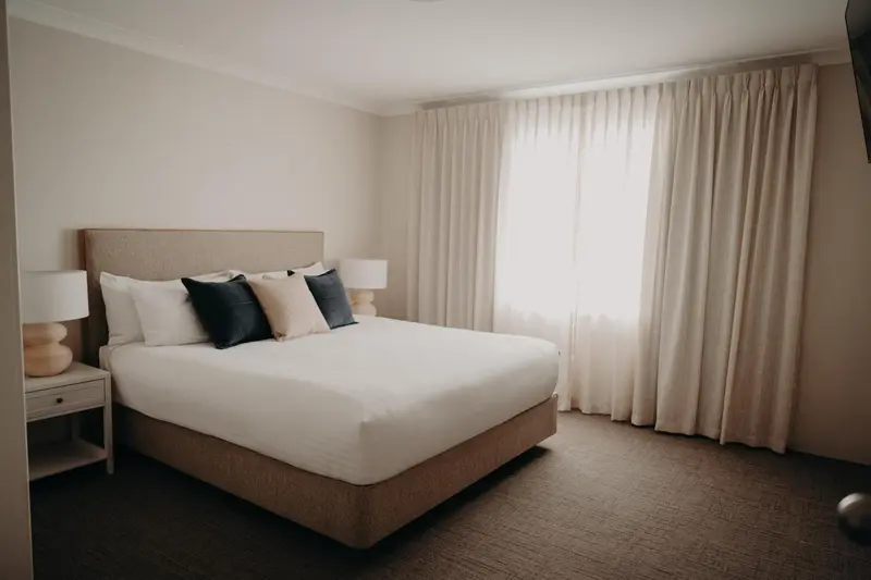 Une chambre lumineuse avec un grand lit et des rideaux clairs.