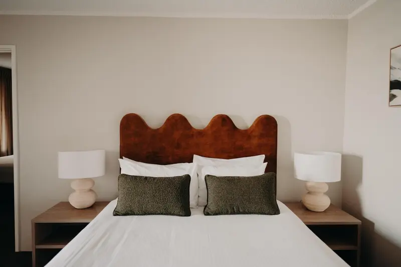 Un lit avec une tête de lit en velours brun et deux lampes de chevet.