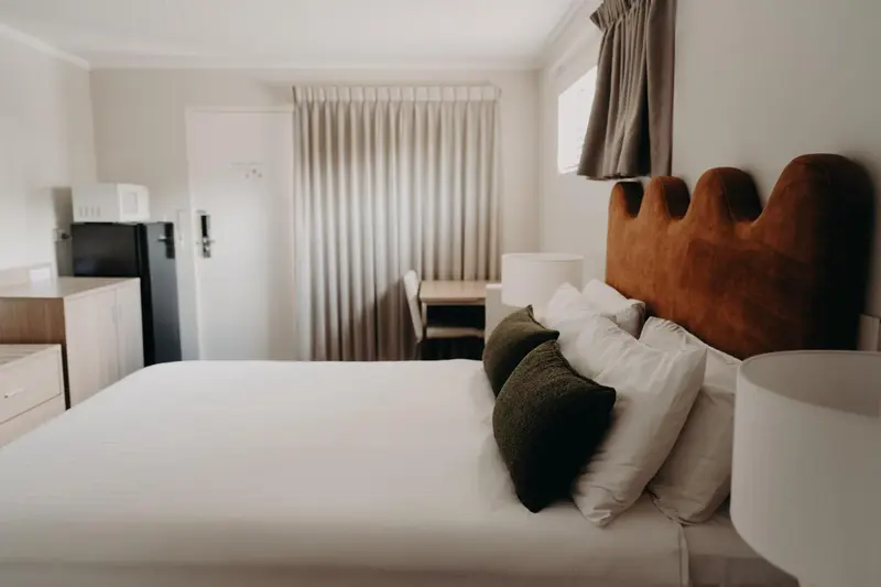 Une chambre lumineuse avec un lit recouvert d'oreillers et une kitchenette.