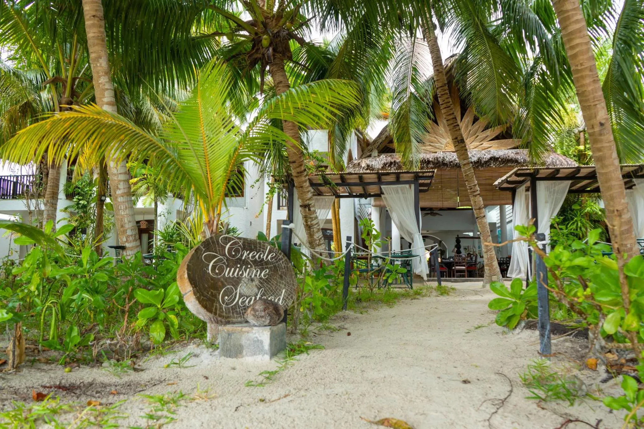 Une entrée ombragée mène à un restaurant en bord de mer.