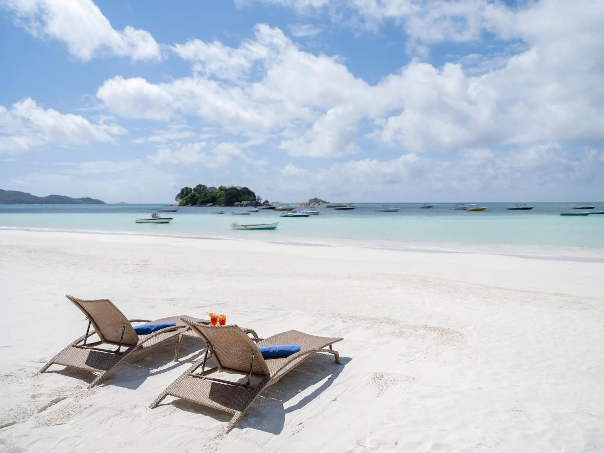Deux transats avec des boissons sur une plage de sable blanc.