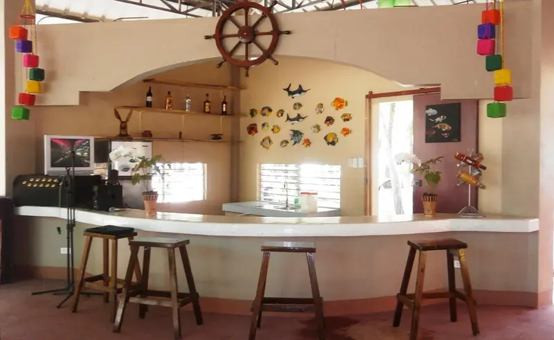 Un comptoir de bar en bois clair est bordé de tabourets hauts dans une pièce décorée de motifs marins.