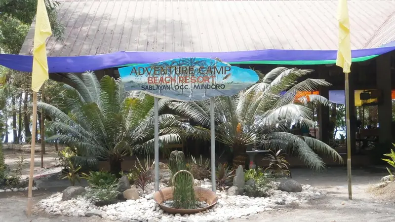 Entree d'un complexe touristier tropical avec vegetation et panneaux.