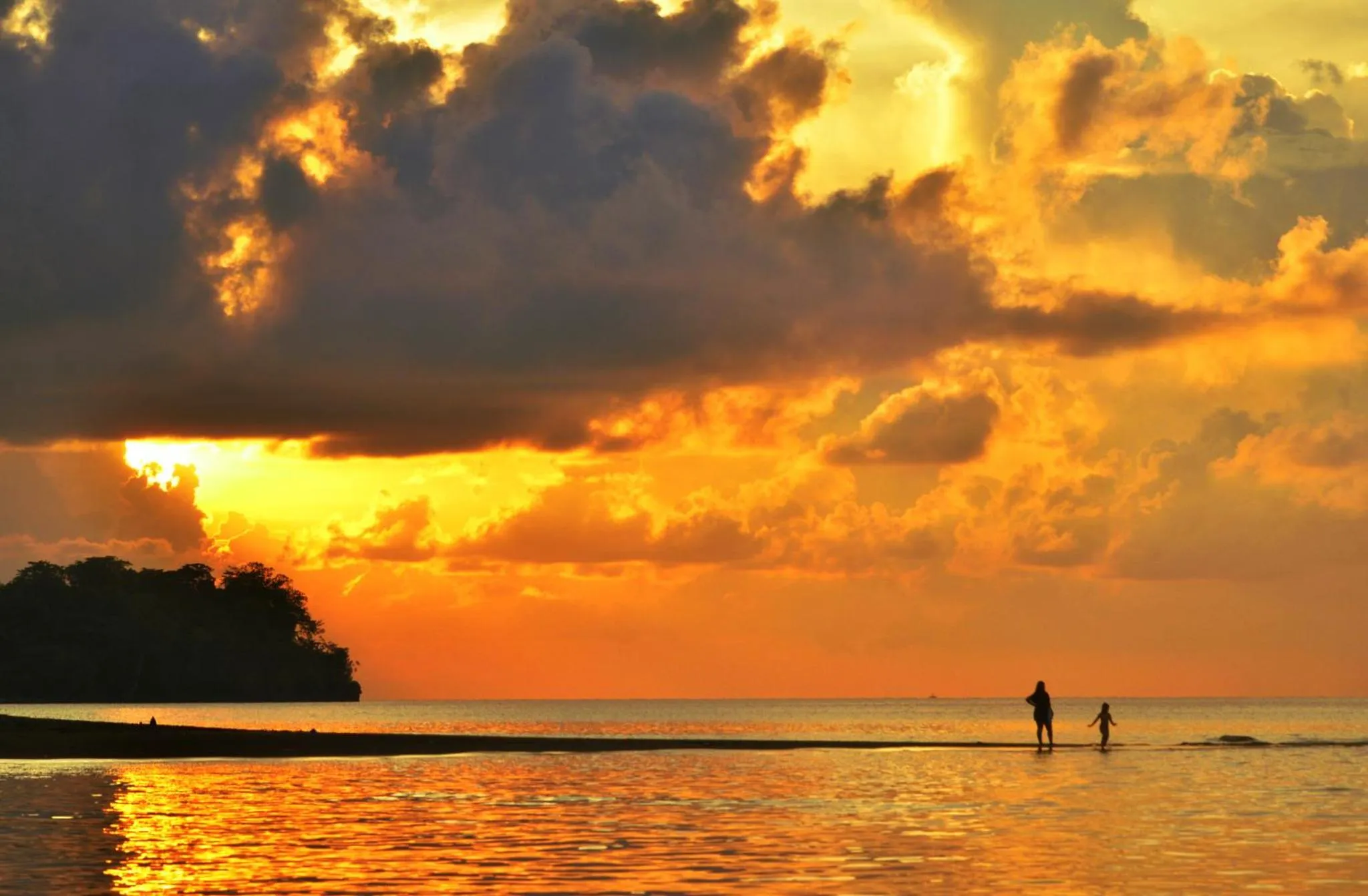 Coucher de soleil sur une plage avec deux silhouettes marchant dans l'eau.